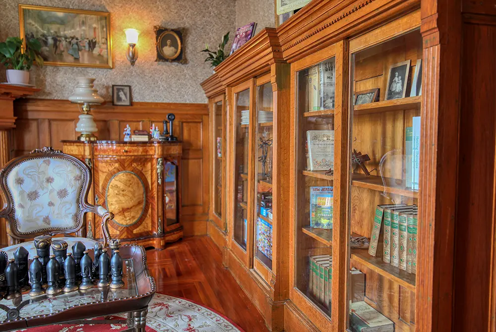 A vintage study in a Toms River historic inn features wooden bookshelves filled with books and decor, a chessboard on a table, ornate chairs, and classic wall art in a warmly lit, elegant room.