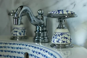 Close-up of a bathroom faucet and handles with ornate blue floral patterns on white porcelain, set against a marble background—an elegant detail found in Toms River NJ bed and breakfast rooms.